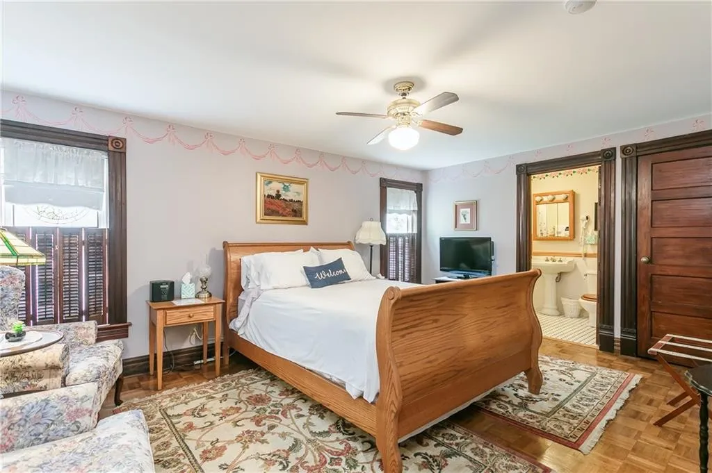 Cozy bedroom featuring a wooden sleigh bed, floral armchair, and a TV. Includes an ensuite bathroom and warm decor, ideal for relaxation.