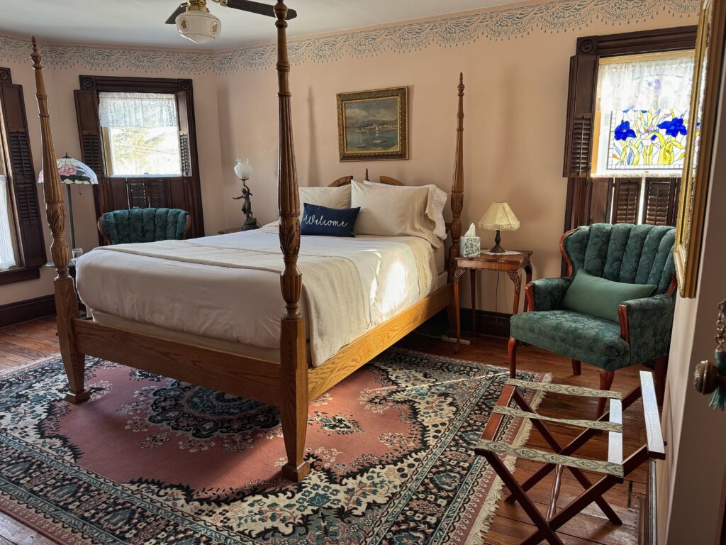 Cozy bedroom featuring a four-poster bed, vintage furnishings, and a stained glass window, creating a welcoming, relaxed atmosphere.